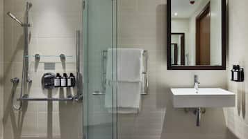 Un baño moderno con ducha de vidrio, un lavamanos blanco y un espejo grande.