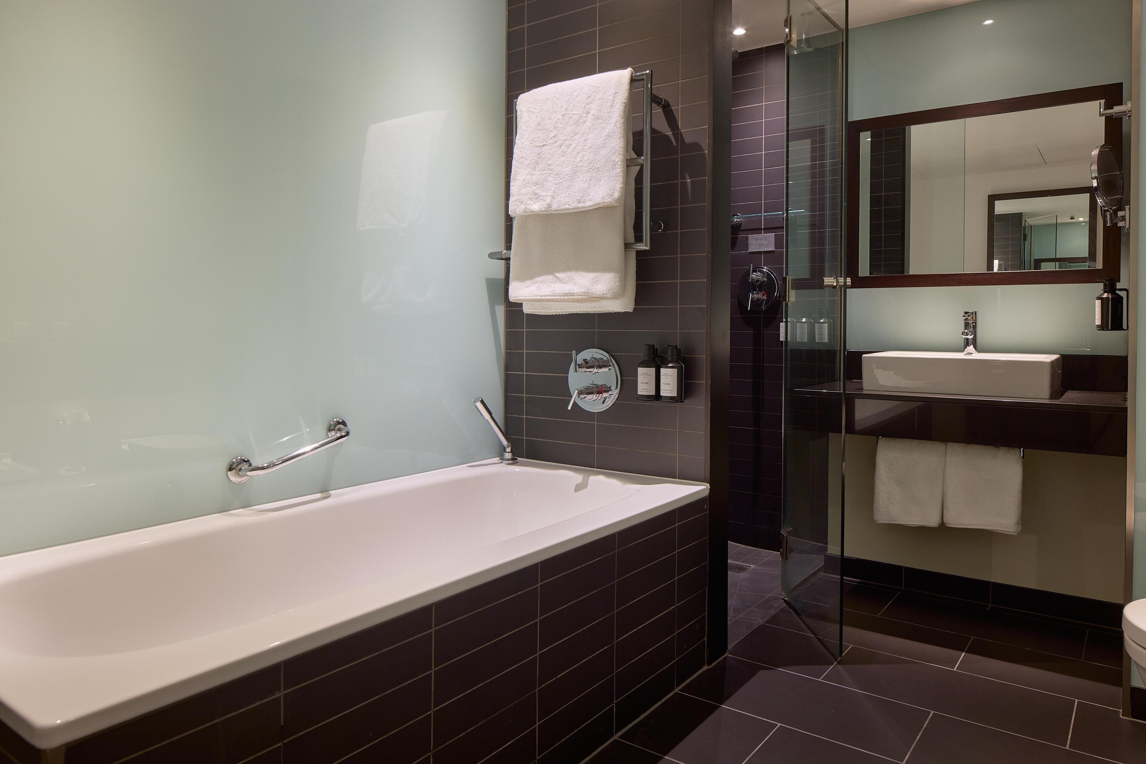 A modern bathroom with a bathtub, a glass shower enclosure, a sink, and a large mirror.