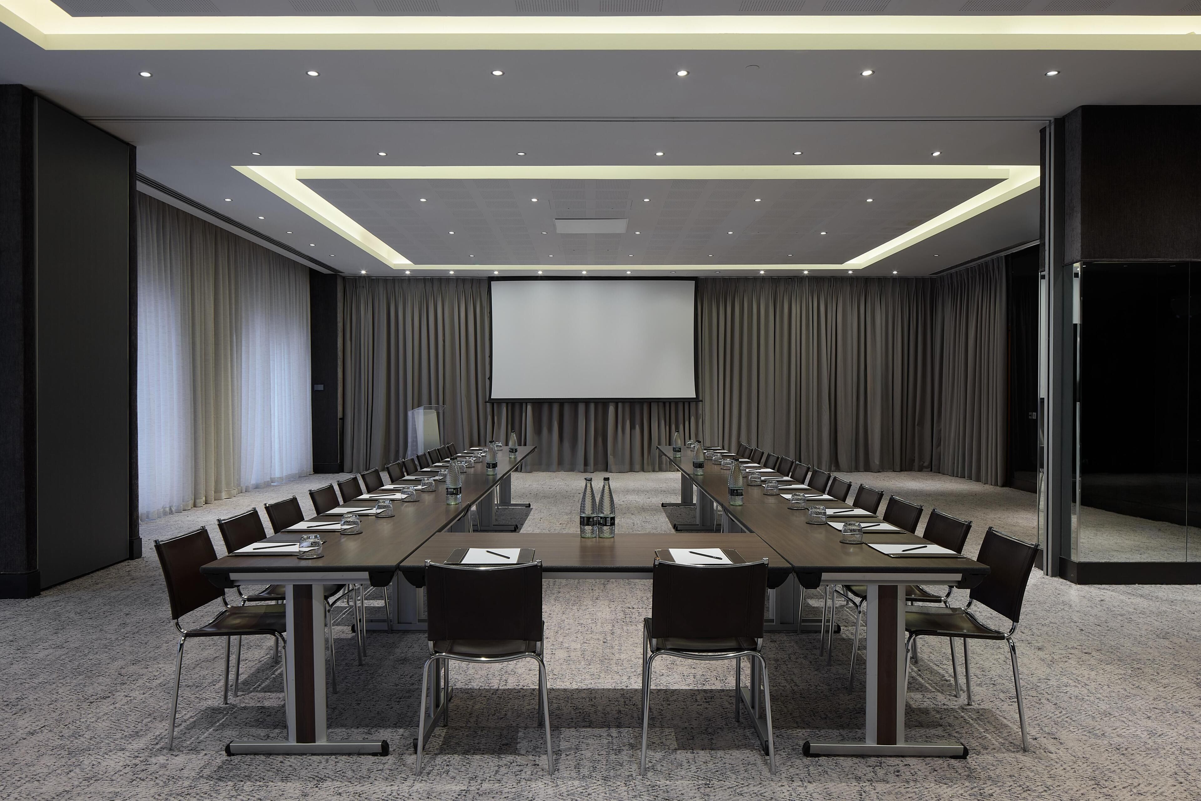 A conference room with a long table, chairs, a projector screen, and a carpeted floor.