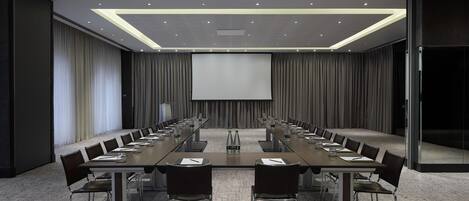 A conference room with a long table, chairs, a projector screen, and a carpeted floor.