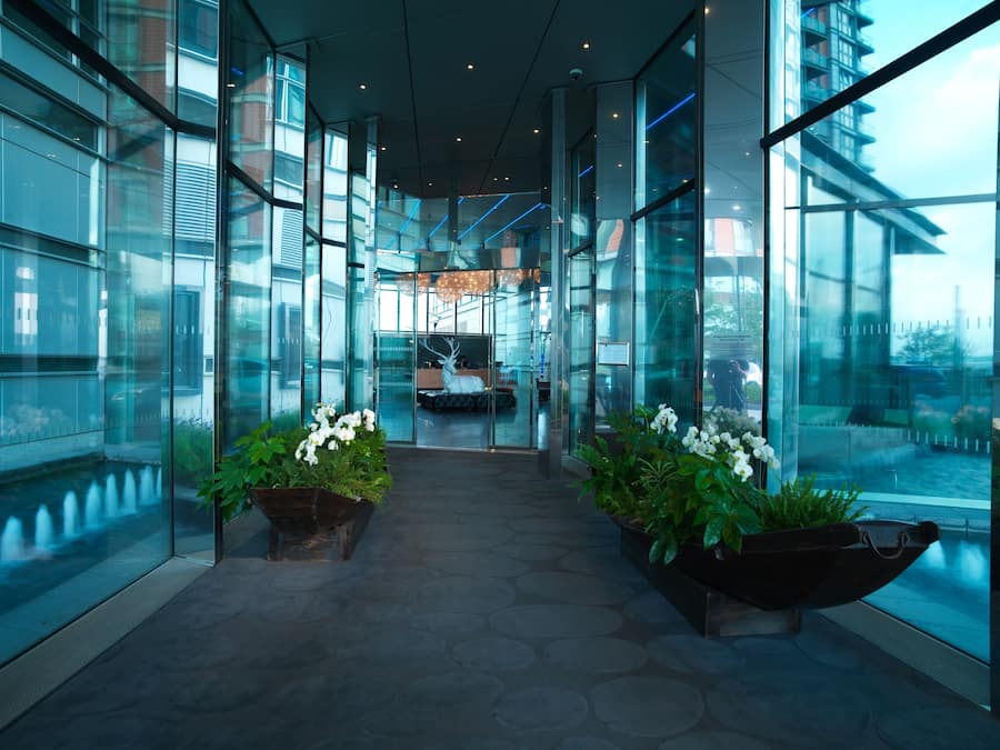 Un hall d’hôtel moderne avec des murs en verre, un escalier central et des plantes en pot.