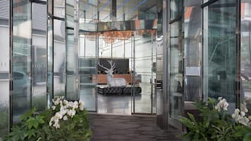 A modern hotel lobby with glass walls, a central seating area, and a chandelier.