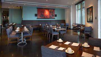 Un restaurant doté de nombreuses tables et chaises, d’un grand tableau accroché au mur et offrant une vue sur l’extérieur grâce à de grandes fenêtres.