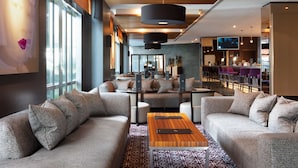 A modern hotel lobby with a sofa set, a wooden coffee table, and a bar area with purple chairs. - Radisson Blu Hotel, London Canary Wharf East (London)