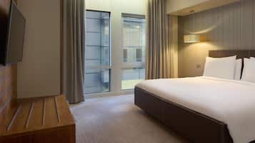 A hotel room with a large bed, a wooden dresser, a flat-screen TV, and a sliding glass door leading to a balcony.