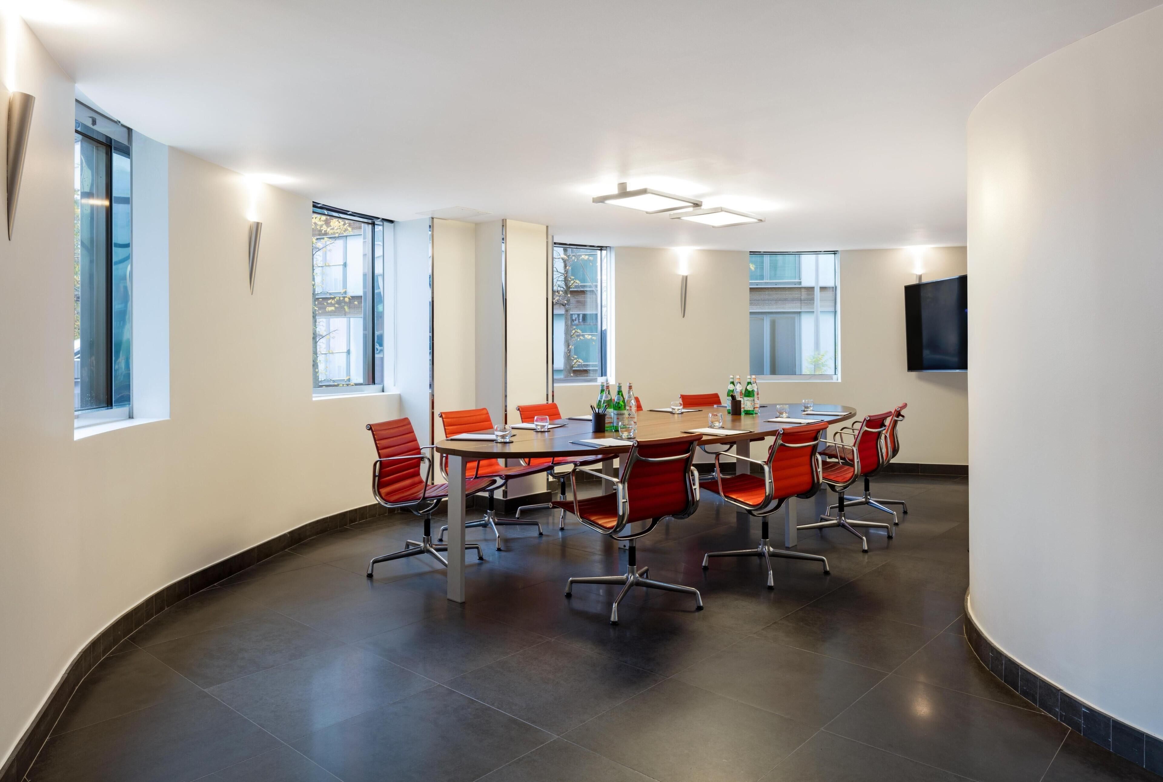 A conference room with a round table, red chairs, and large windows.