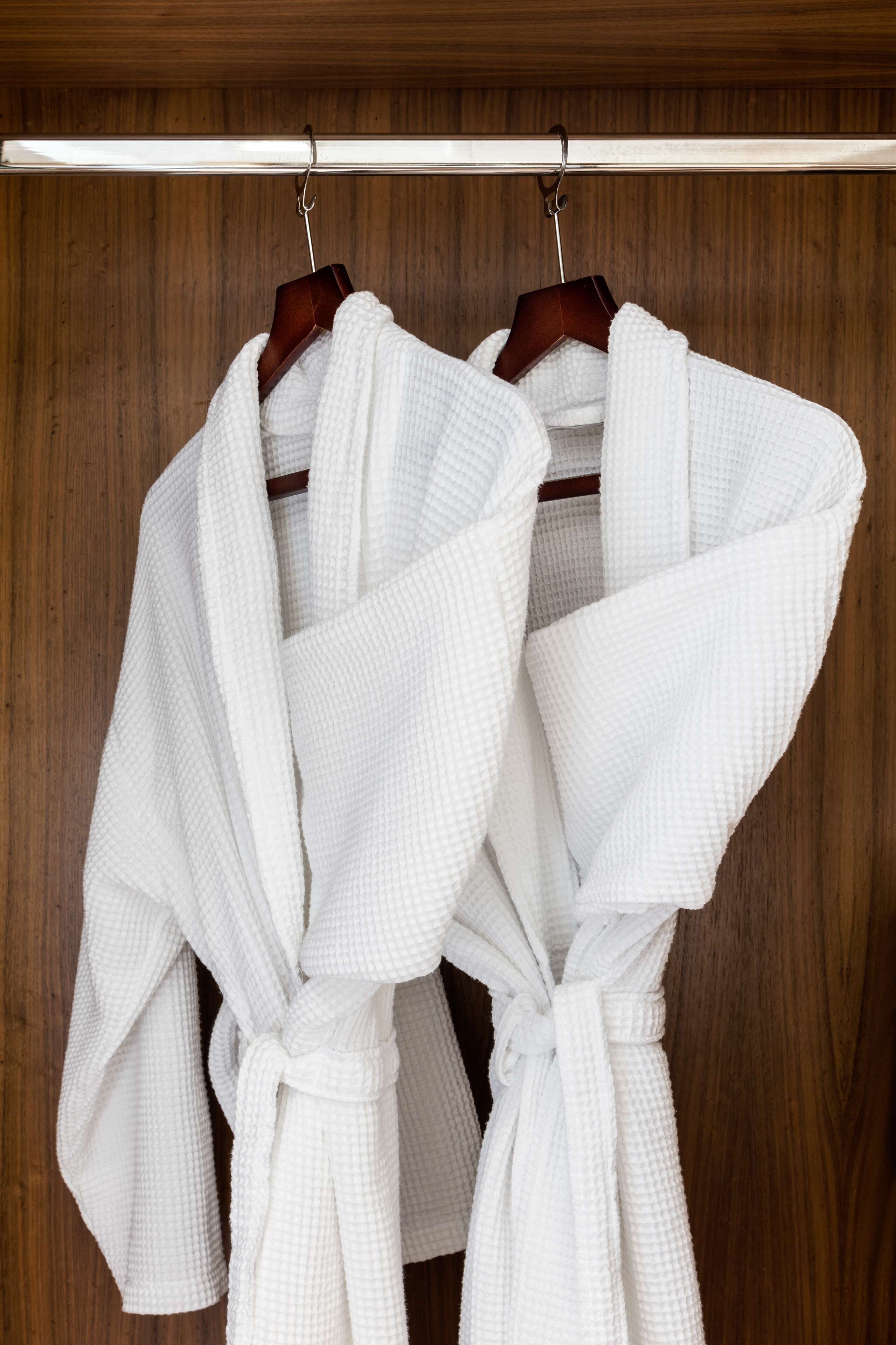 Two white bathrobes hanging on a wooden rack.
