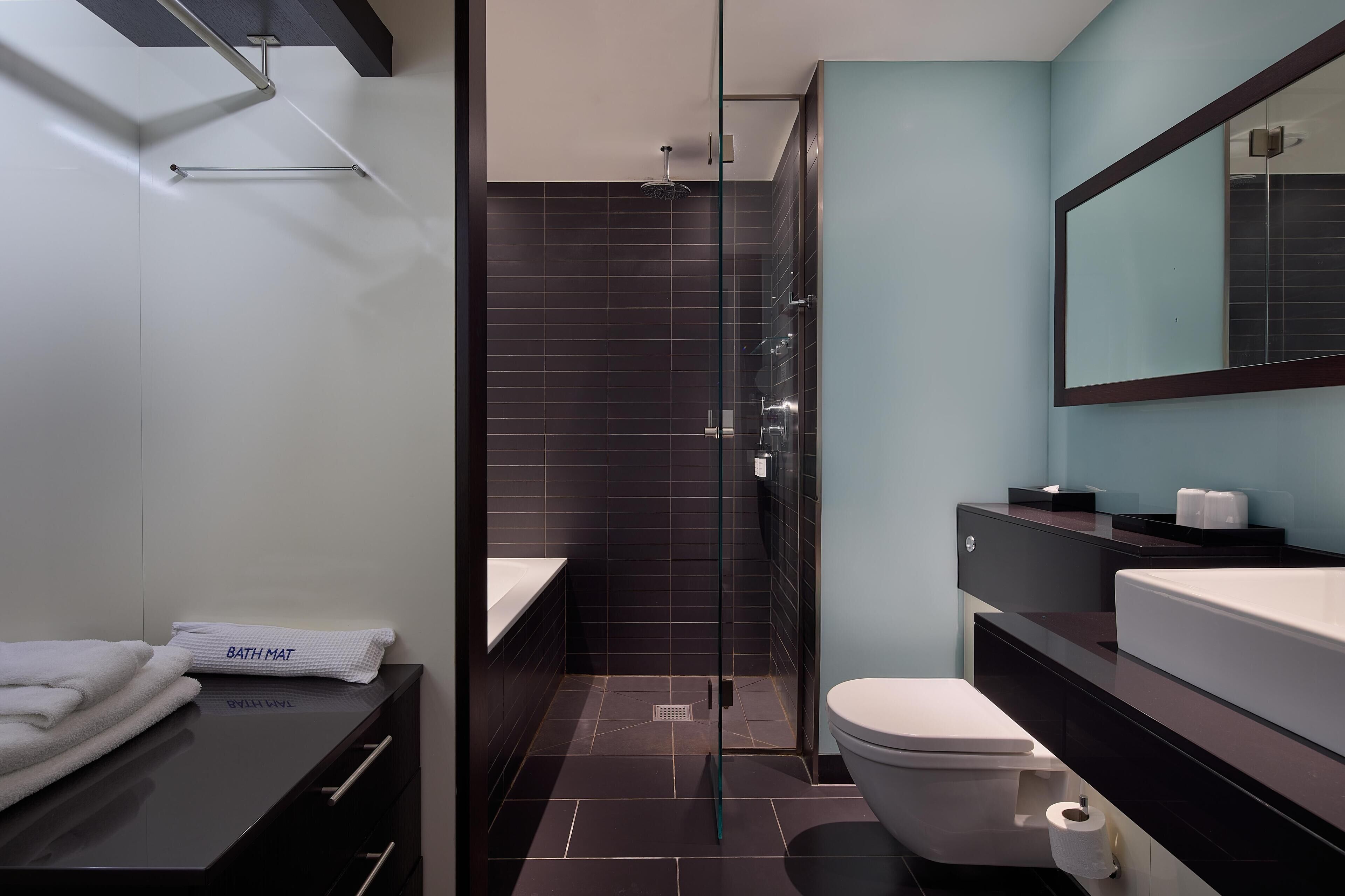 Un baño moderno con cabina de ducha de vidrio, pared de azulejos oscuros, lavamanos blanco y un espejo grande.
