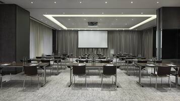 Ein Konferenzraum mit mehreren Tischen und Stühlen, einer großen Leinwand und einem Teppichboden.