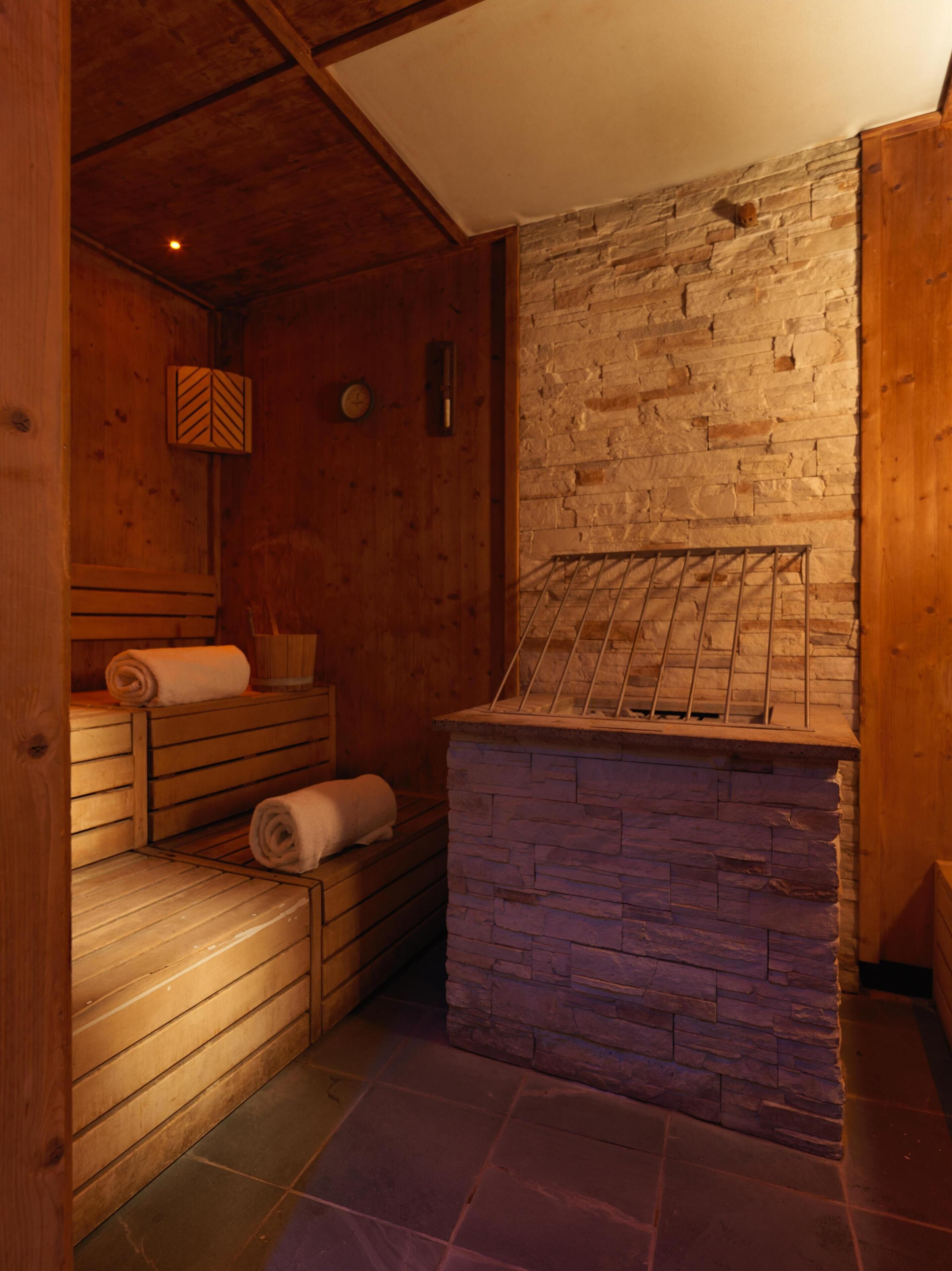 A sauna room with wooden benches, a stone wall, and a tiled floor.