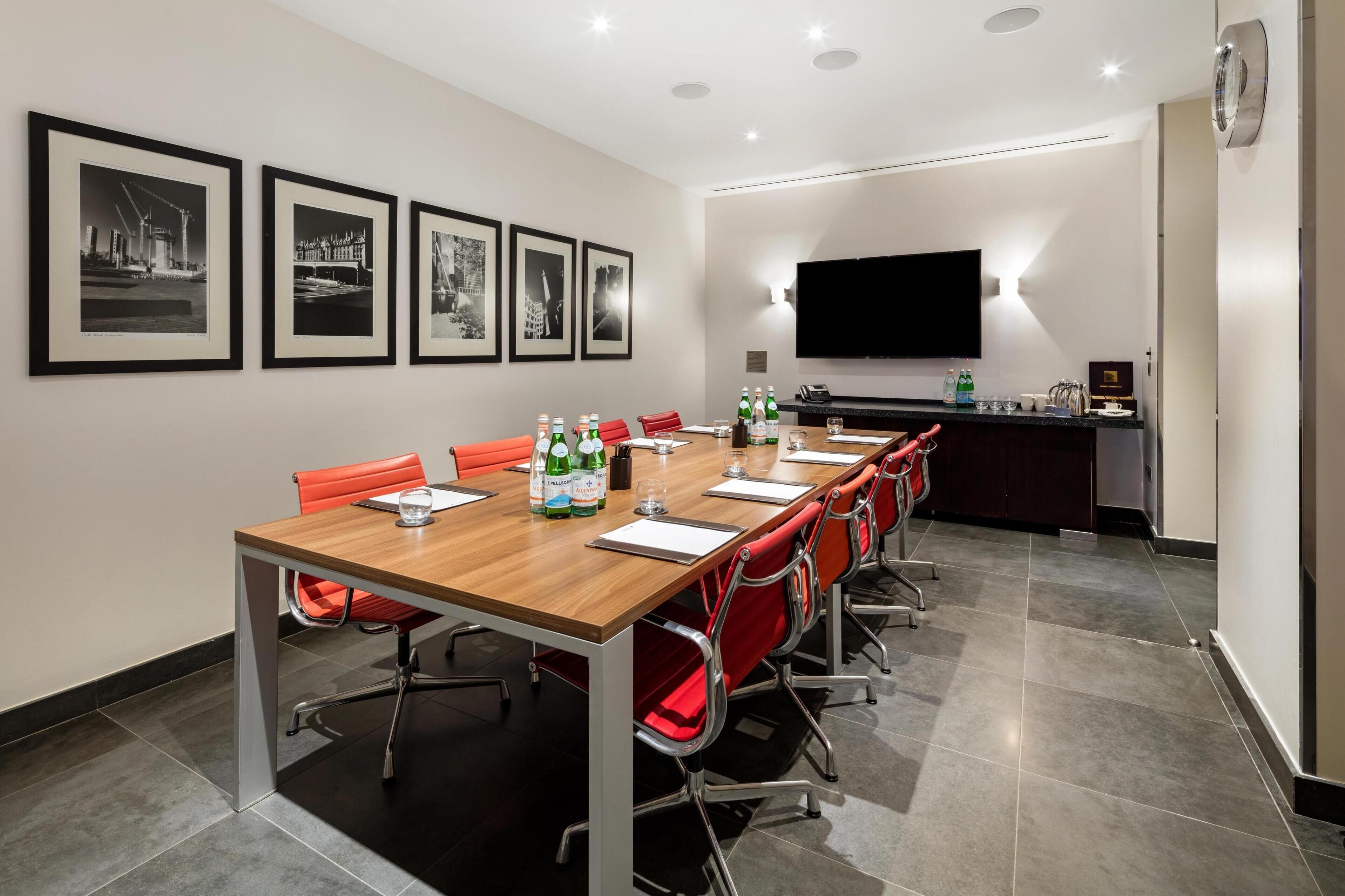 A conference room with a long table, red chairs, a flat-screen TV, and framed pictures on the wall.