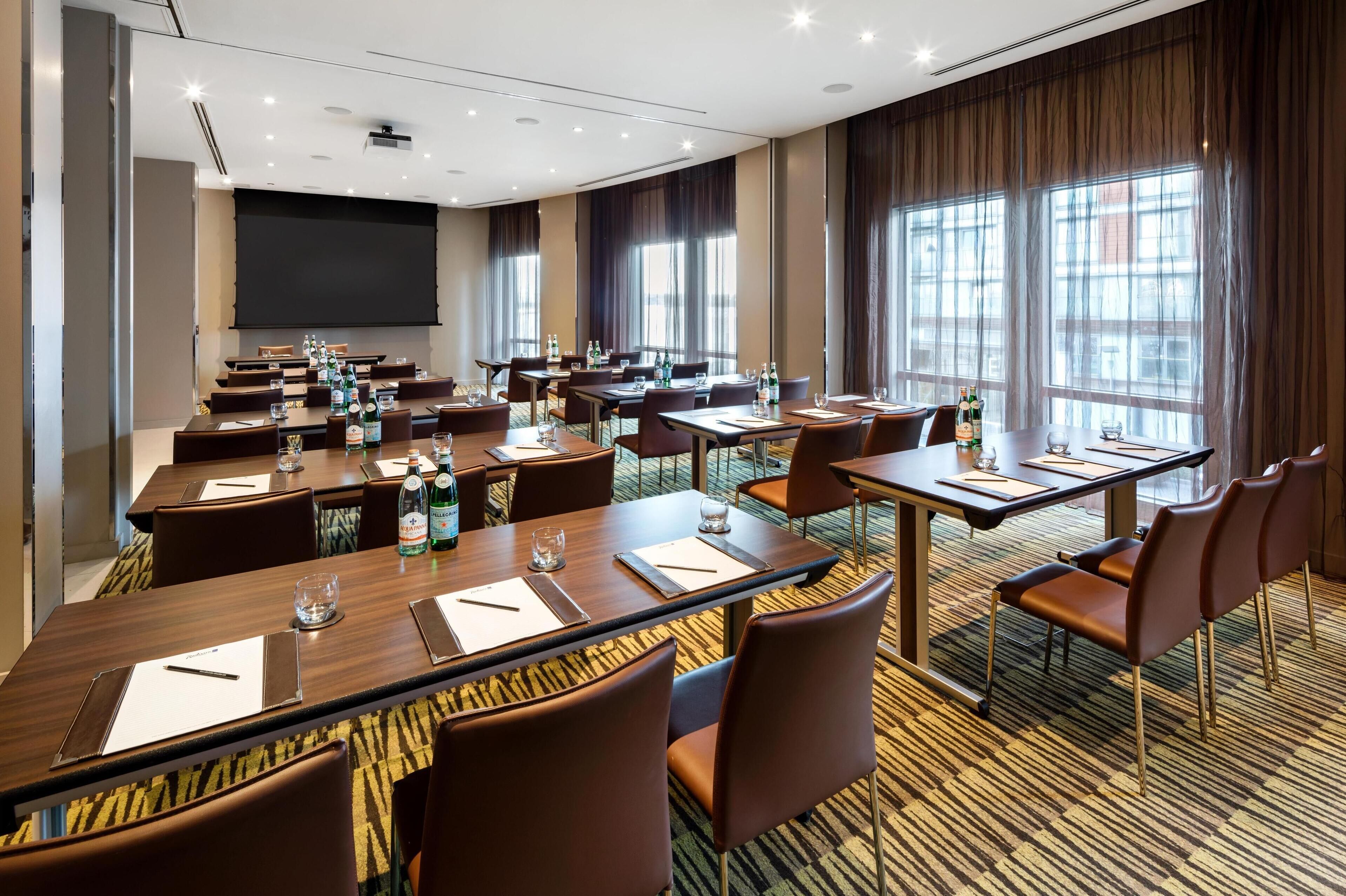 Een vergaderzaal met meerdere tafels, stoelen en een groot scherm.
