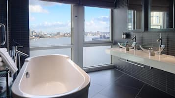 Une salle de bain moderne avec une grande baignoire, un lavabo en verre et une vue sur la ville grâce à de grandes fenêtres.