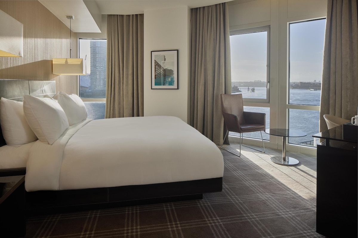 A hotel room with a large bed, a chair, a small table, and a view of the water.