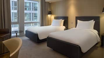 A hotel room with two beds, a glass table, a chair, and large windows with curtains.
