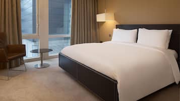 A hotel room with a large bed, a chair, a small table, and a window with curtains.