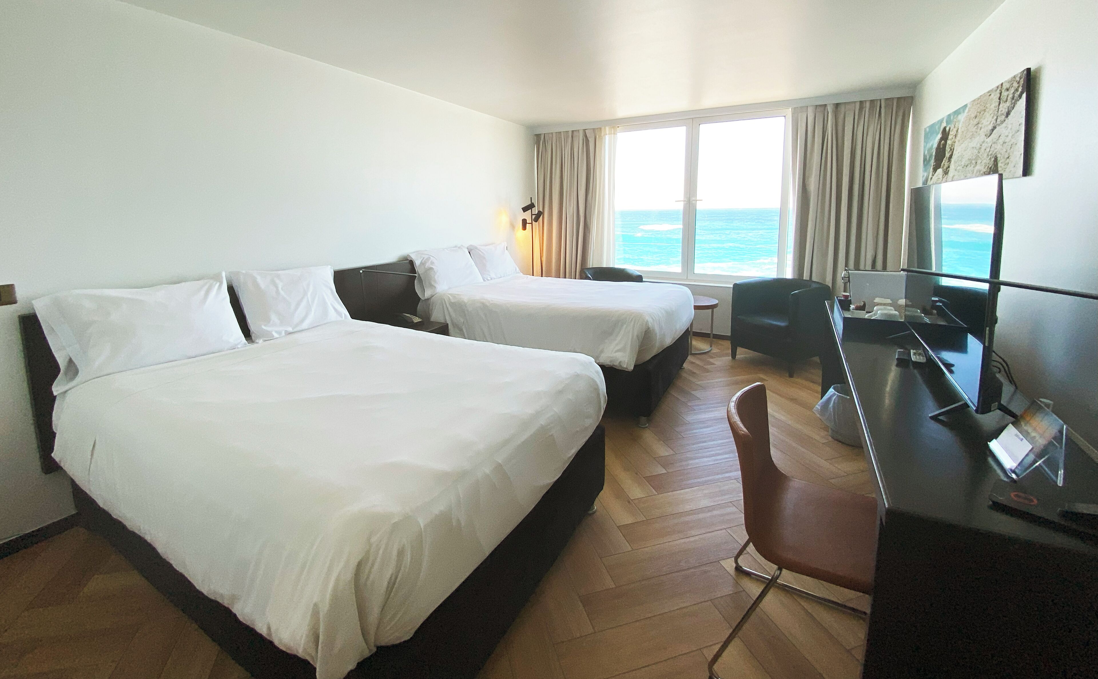 A hotel room with two beds, a desk with a computer, a chair, and a view of the ocean.