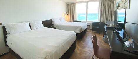 A hotel room with two beds, a desk with a computer, a chair, and a view of the ocean.