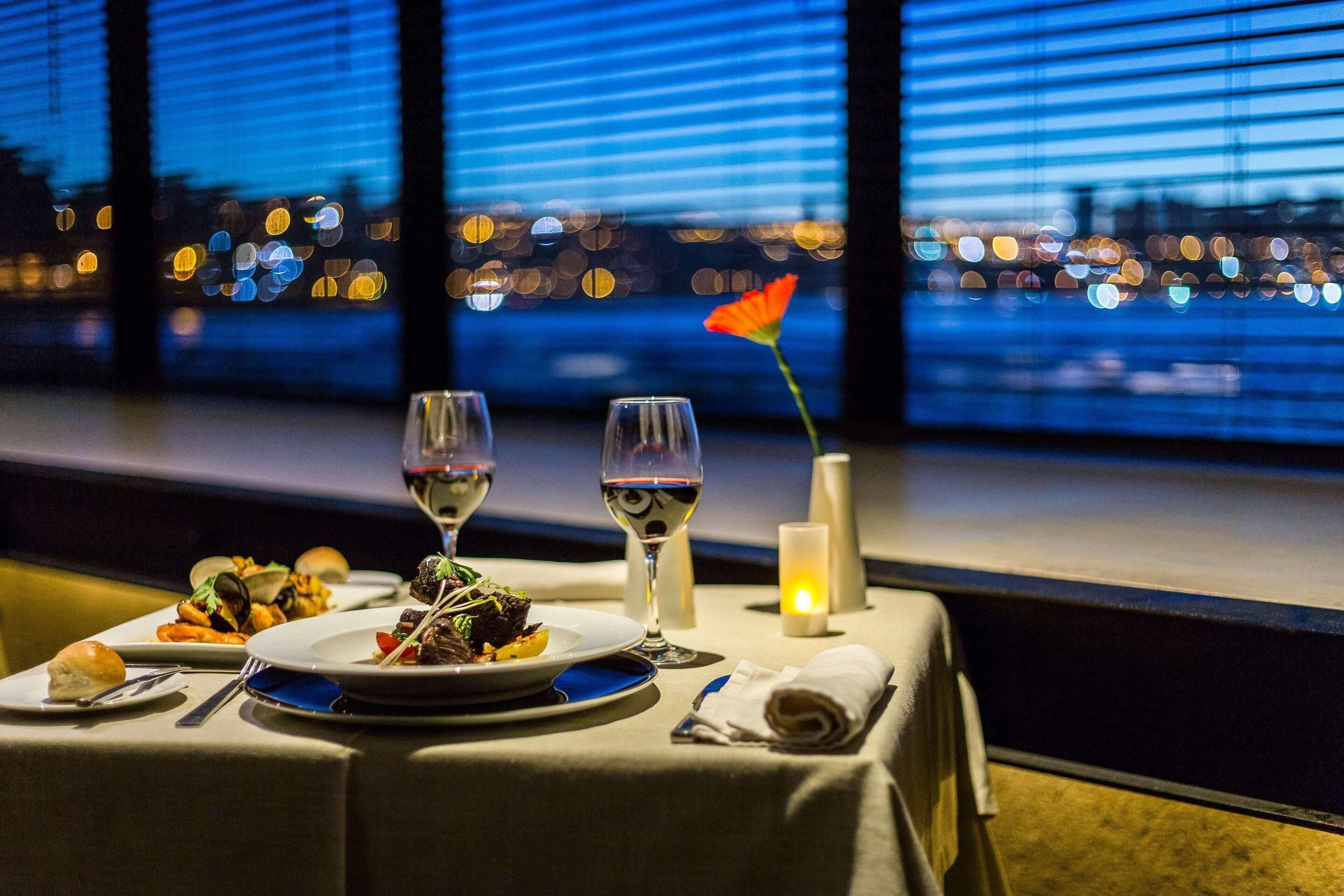 A table set for two with plates of food, two wine glasses, a candle, and a single flower.