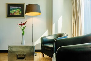 Una habitación con un sofá de cuero negro, una lámpara de pie, un cuadro enmarco y un jarrón con flores sobre una mesa.