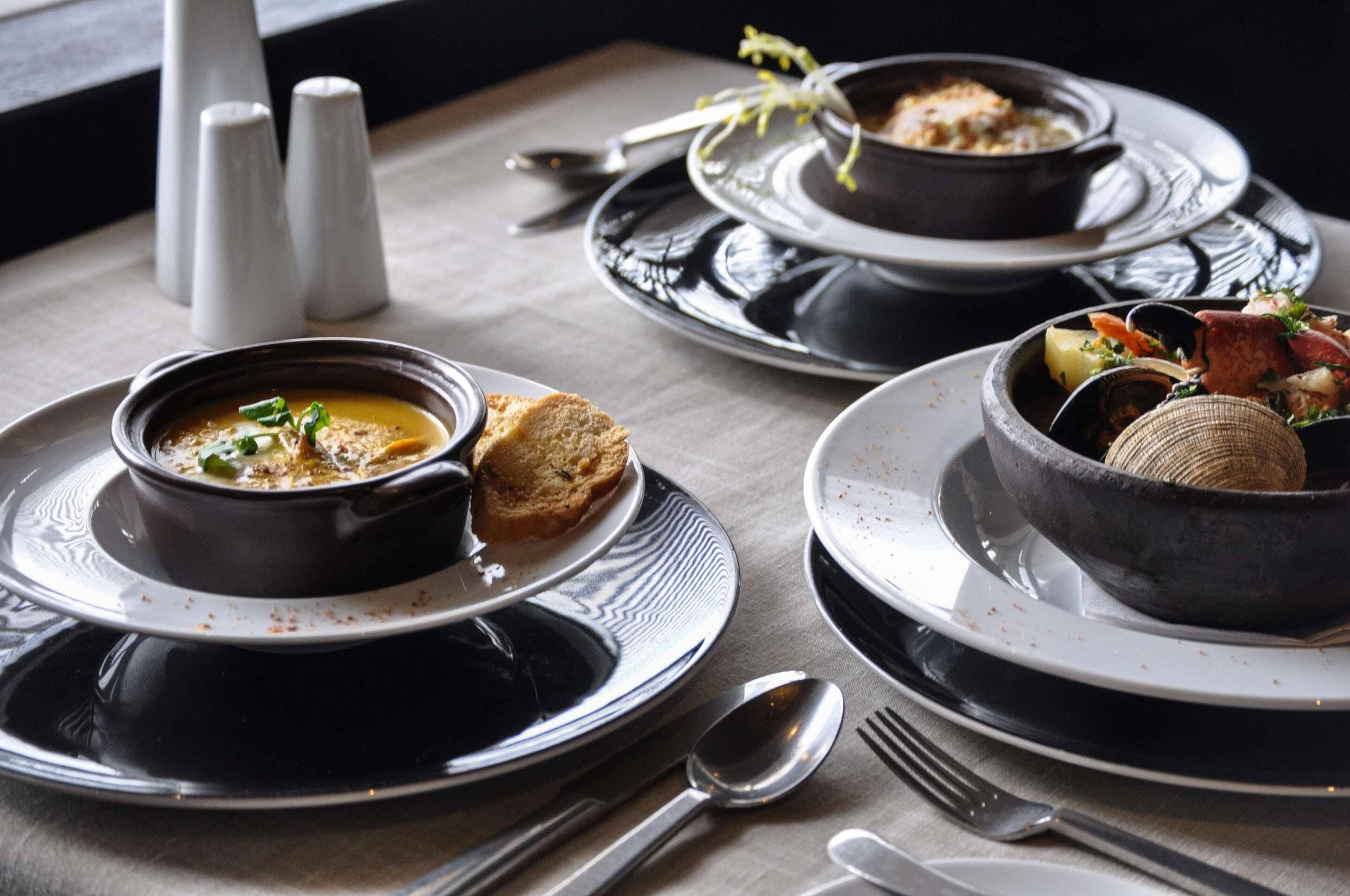 Une table dressée avec trois bols de soupe, chacun garni d’un accompagnement différent, et une assiette de pain.