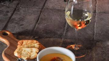A bowl of soup with a spoon and a glass of white wine on a wooden board, with a fire in the background.
