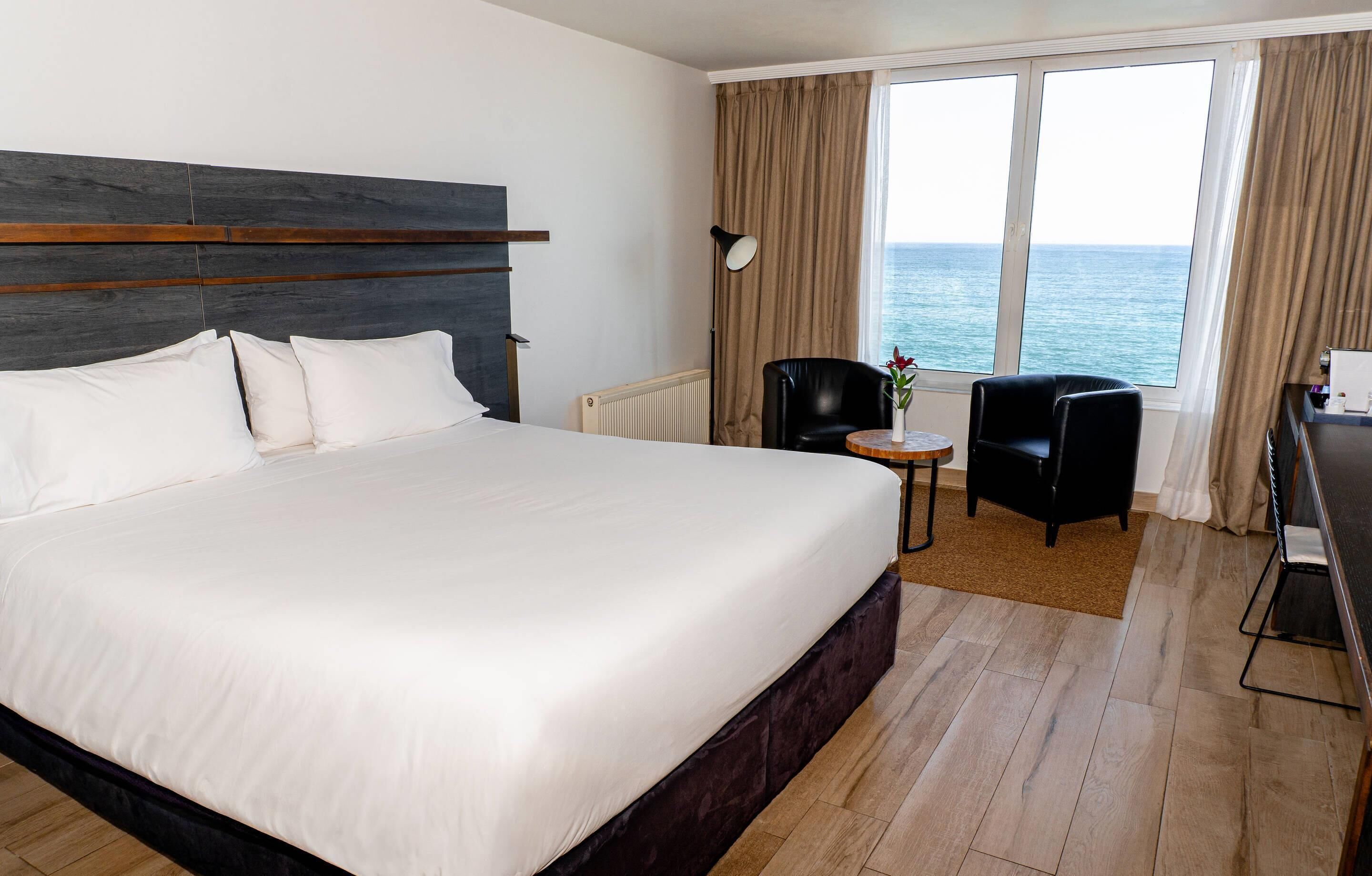 Camera d'albergo con un letto grande, una scrivania, una sedia e vista mare.