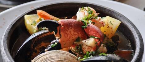 A bowl of seafood stew with clams, mussels, and shrimp, served in a black bowl on a white plate.