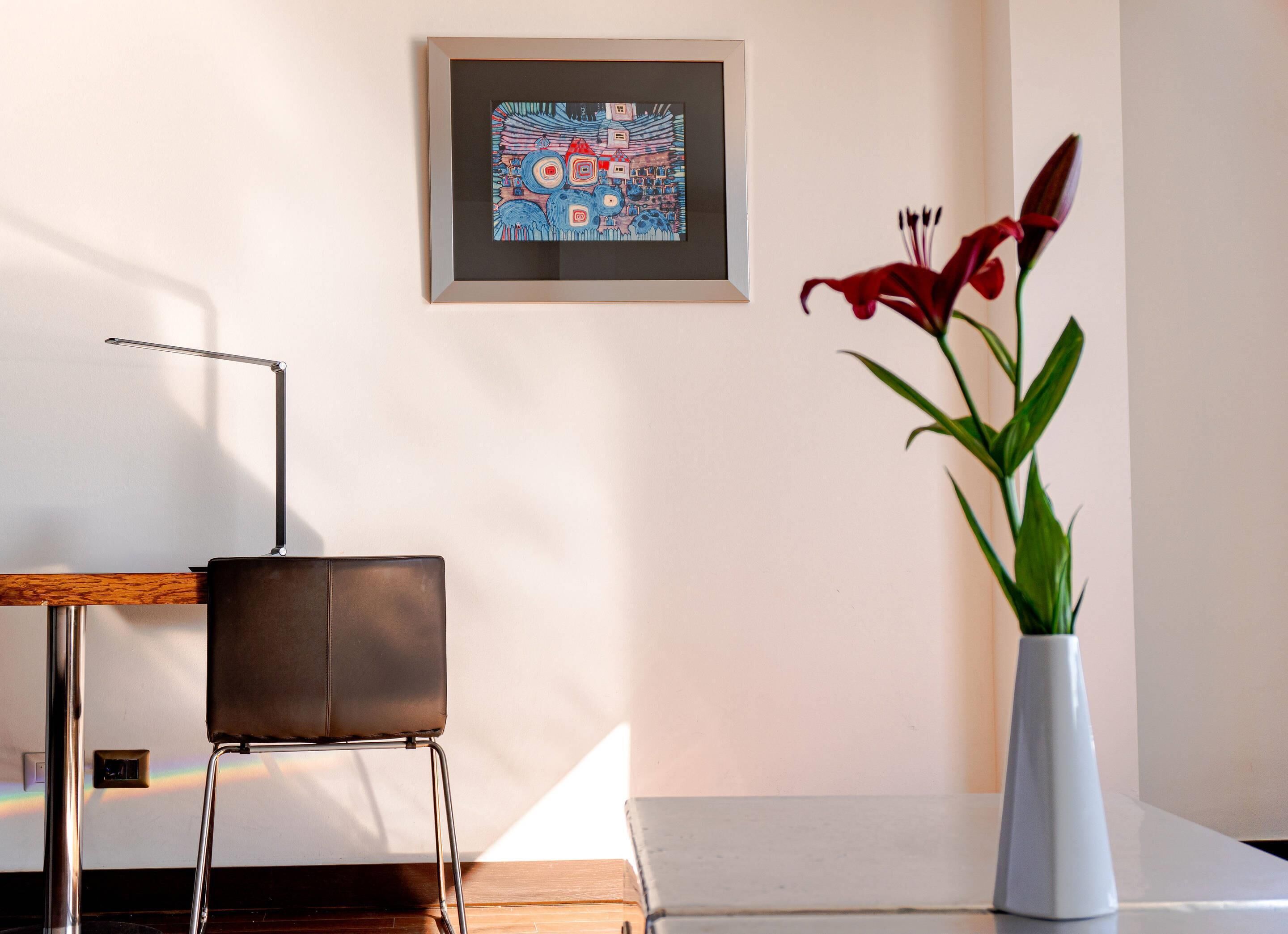 Una habitación moderna con un diseño minimalista, que incluye un escritorio con silla, una obra de arte enmarcada en la pared y un jarrón con flores.