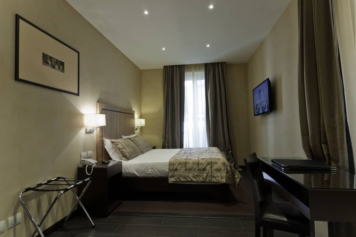 Habitación de hotel con cama, escritorio, silla, lámpara y televisión.