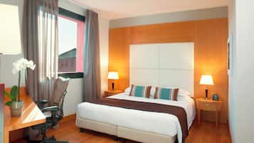 Habitación de hotel con una cama grande, dos mesitas de noche con lámparas, un escritorio con silla y una ventana con cortinas.