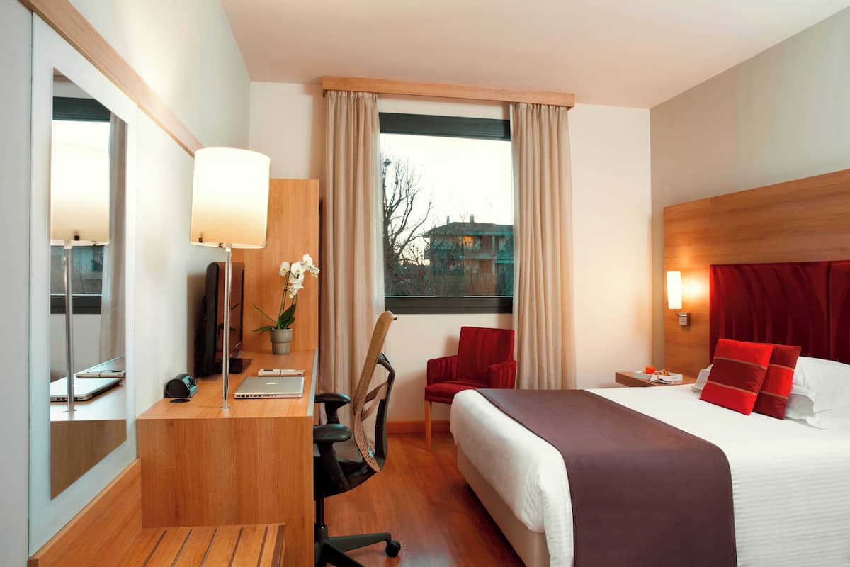 Una camera d'albergo con un letto, una scrivania, una sedia e una finestra con tende.
