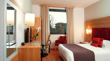 A hotel room with a bed, desk, chair, and a window with curtains.