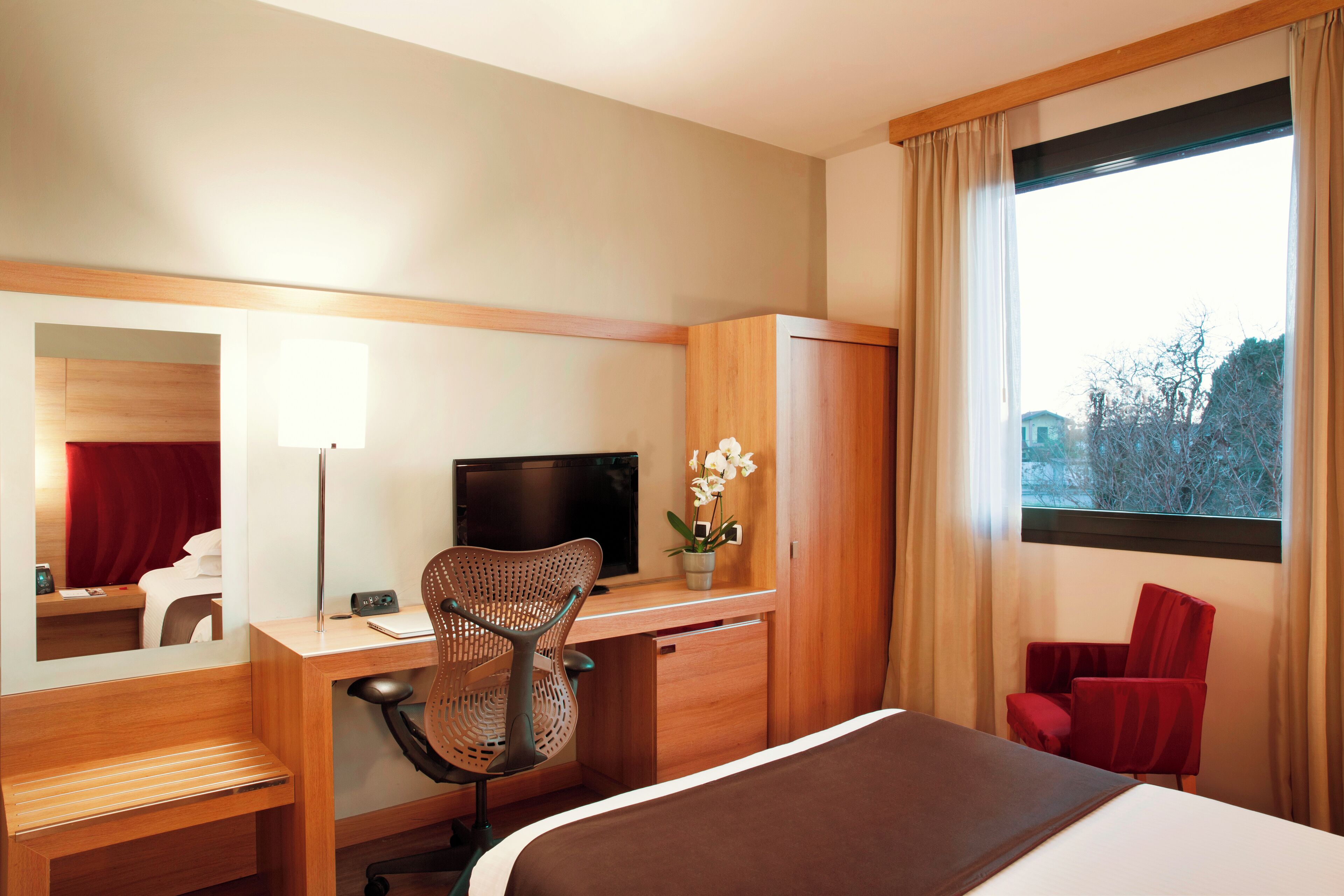 A hotel room with a bed, desk, chair, TV, and a window with curtains.