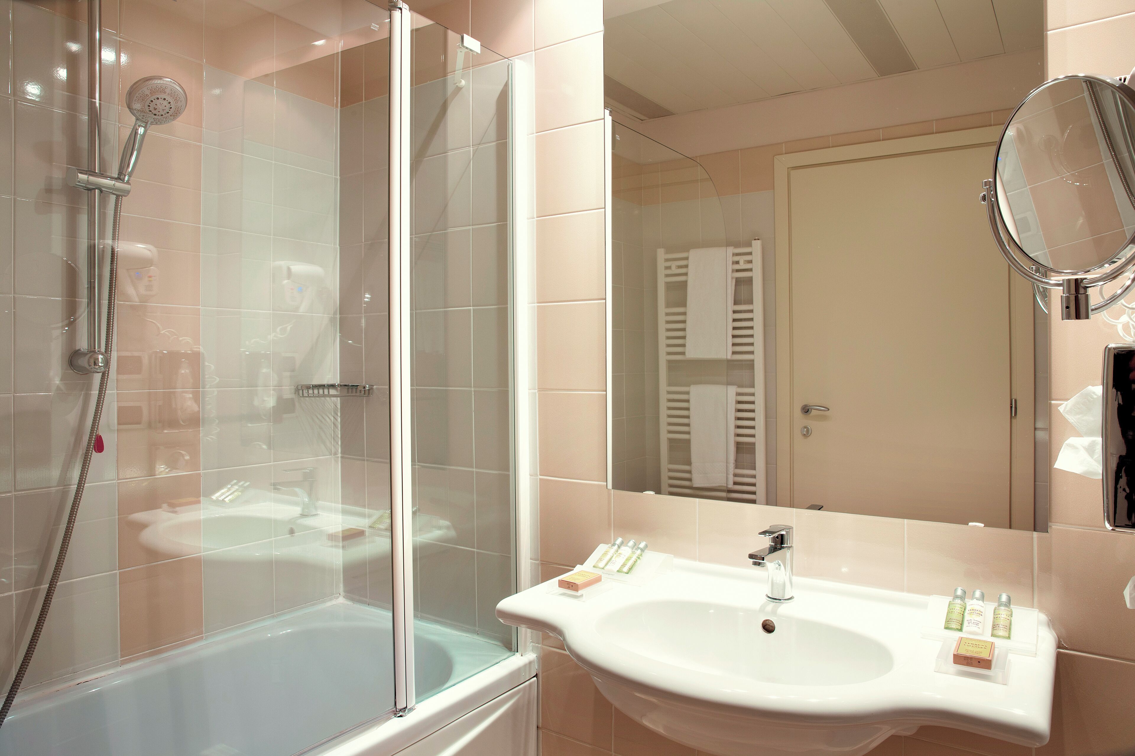 A bathroom with a glass-enclosed shower, a sink with toiletries, and a mirror.