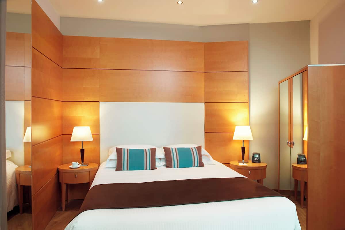 Una camera d'albergo con un letto grande, due comodini con lampade, uno specchio e un armadio.