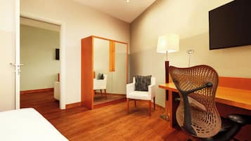 A hotel room with a wooden floor, a bed, a desk with a chair, a mirror, and a TV on the wall.
