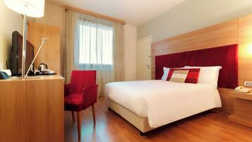 A hotel room with a bed, a desk with a telephone, a chair, a television, and a window with curtains.