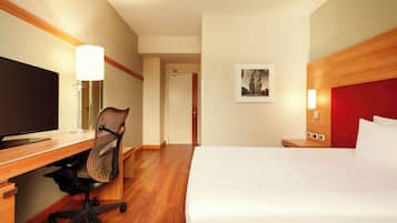 Habitación de hotel con cama, escritorio, silla, televisión y una obra de arte en la pared.