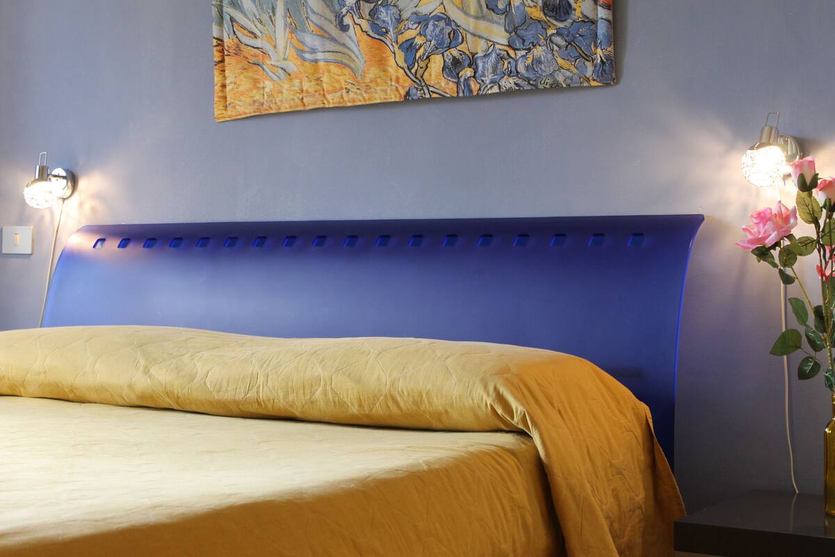 A bedroom with a bed, a headboard, and two wall-mounted lamps.