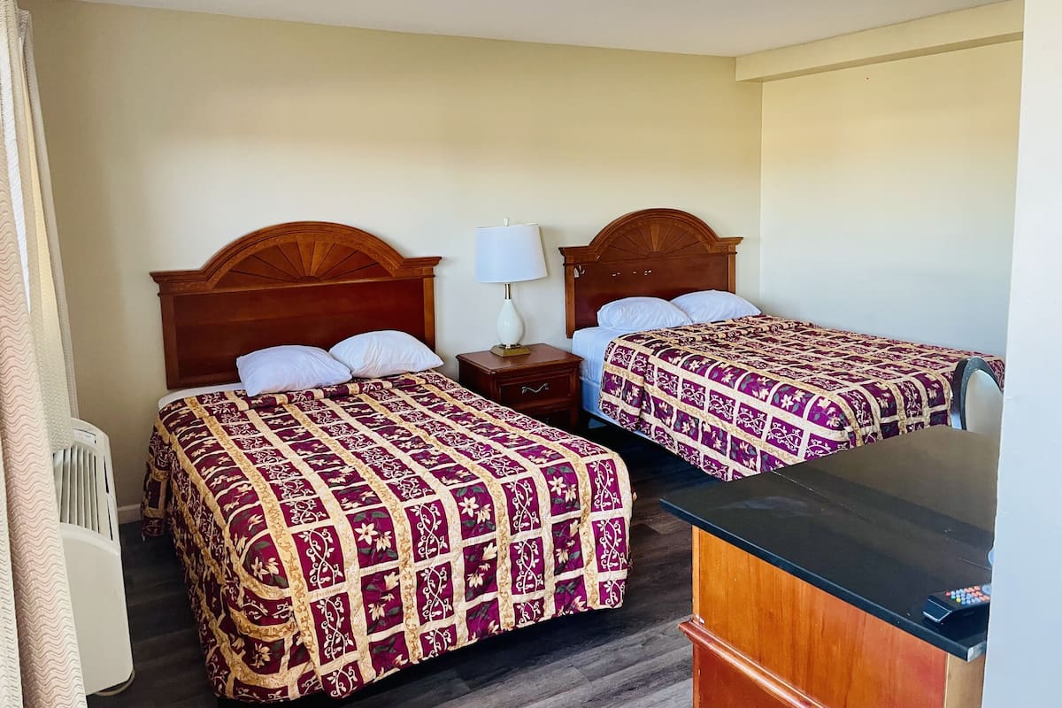 Two single beds with wooden headboards, a bedside table with a lamp, and a desk with a remote control.