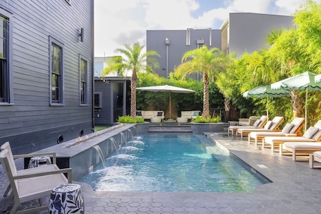 Una piscina al aire libre, sombrillas, sillones reclinables de piscina