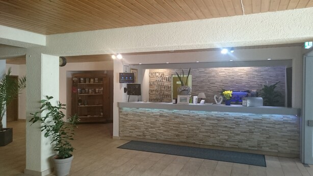 A reception area with a stone-textured counter, a television, and a wall-mounted clock. - Landhotel Wasgau (Hauenstein)