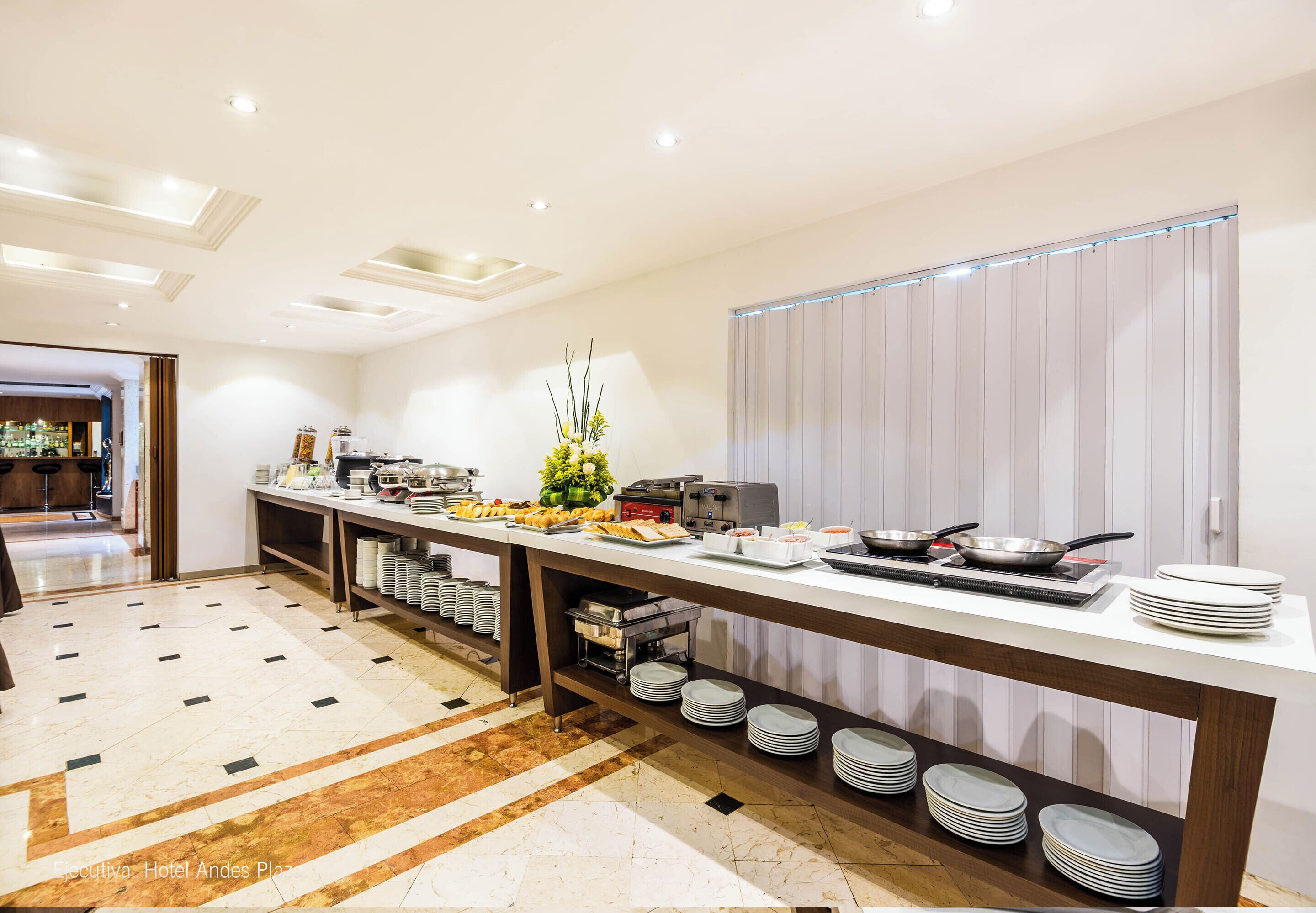 Una cocina de hotel con barra tipo buffet, que incluye una larga mesa con alimentos y una variedad de platos y fuentes.