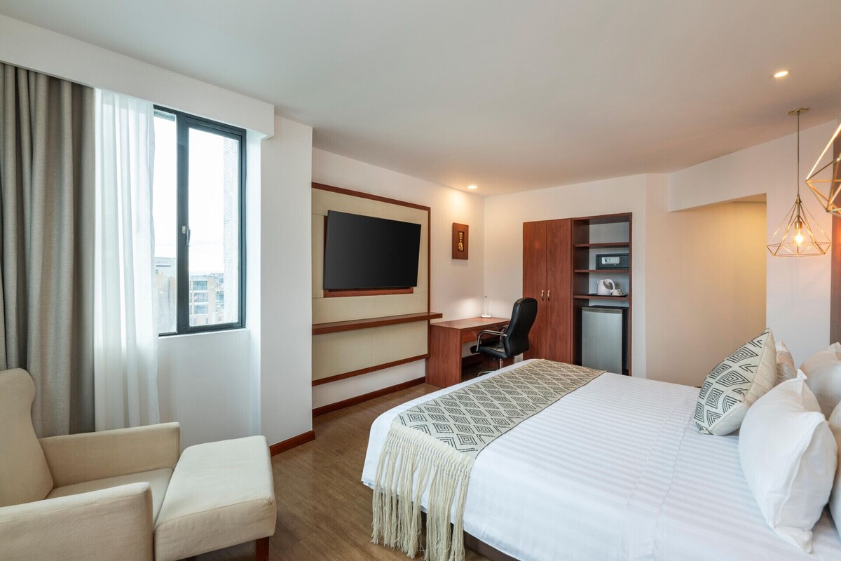 A hotel room with a bed, a desk, a chair, a television, and a wardrobe.