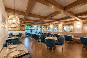 Un interior de restaurante con vigas de madera, sillas tapizadas en azul y lámparas colgantes de ratán.