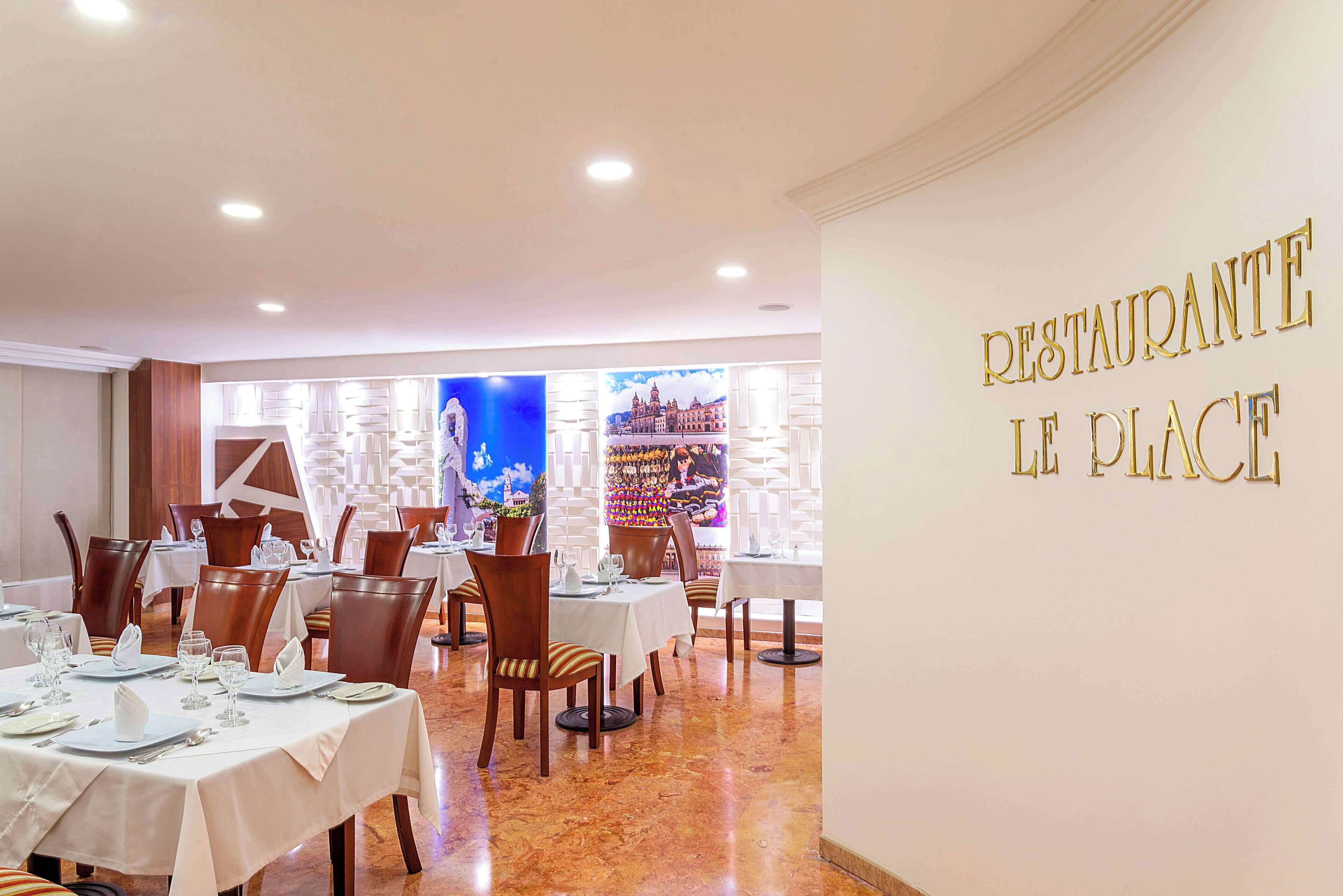 Interior de restaurante con mesas dispuestas para comer, una pared con el rótulo 'RESTAURANTE LE PLACE' y un mural con vista a la ciudad.