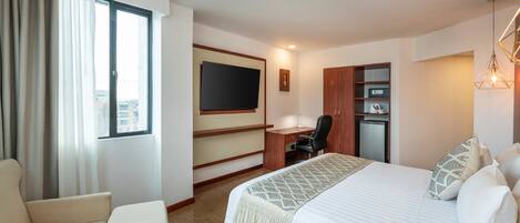 A hotel room with a bed, a desk, a chair, a television, and a minibar.