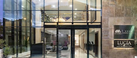 A hotel entrance with a glass facade, a reception area with seating, and a sign for 'EM HOTELS ANDES PLAZA'.