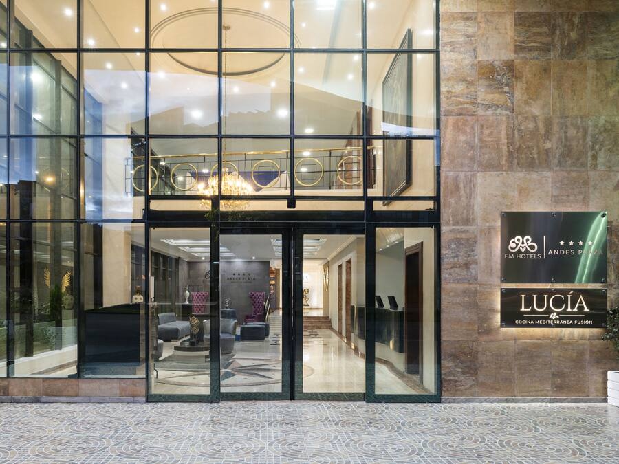 Entrada de hotel com fachada de vidro, área de recepção com assentos e placa com a inscrição 'EM HOTELS ANDES PLAZA'.